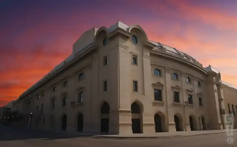 A large tan building with arched doorways and windows against a vibrant purple and orange sunset sky.