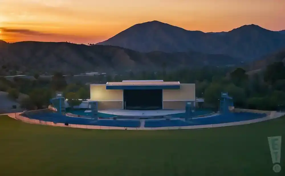 An outdoor amphitheater is illuminated against a sunset with mountains in the background.