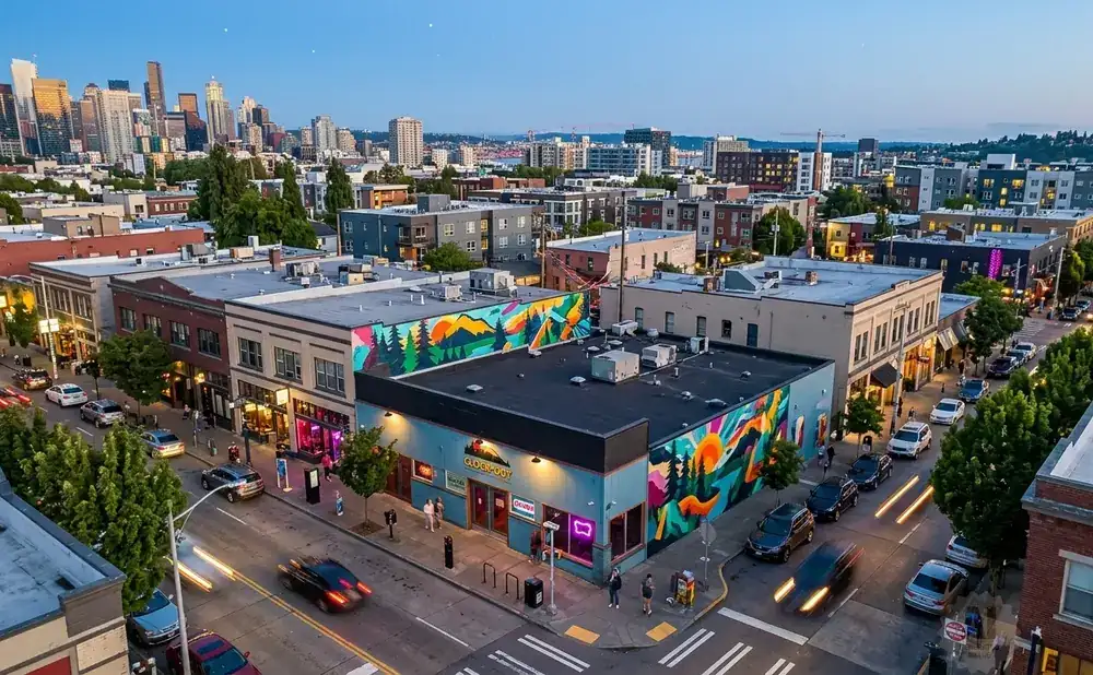 Aerial view of a city street with buildings, cars, and a mural at dusk.