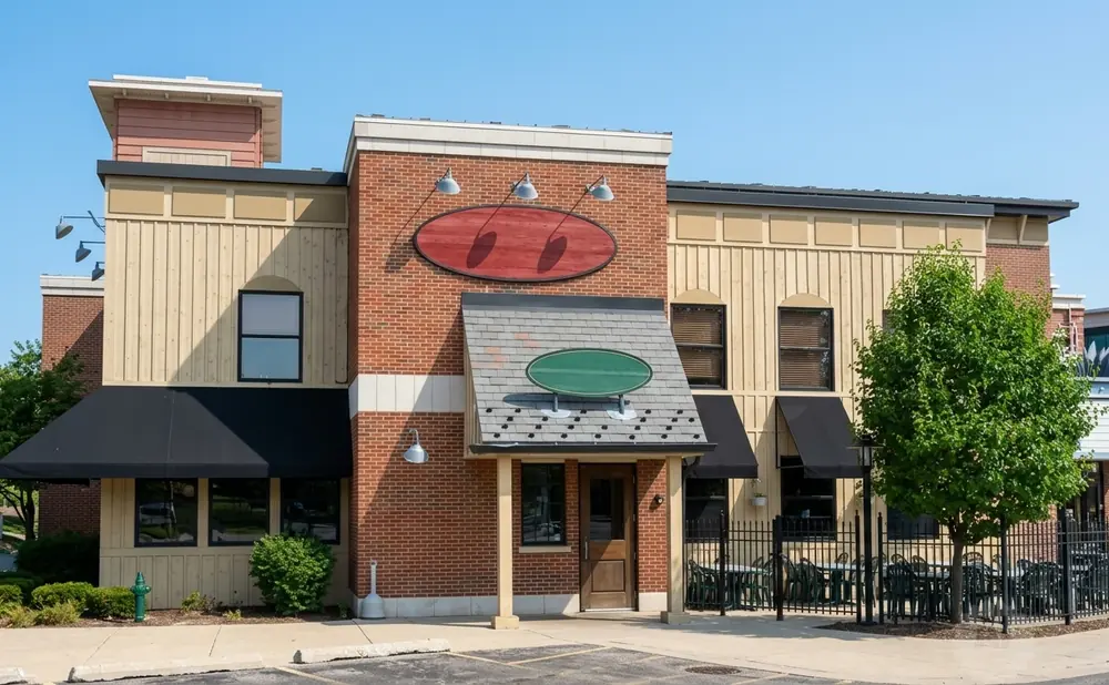 A brick and wood-sided building with black awnings and outdoor seating under a clear blue sky.