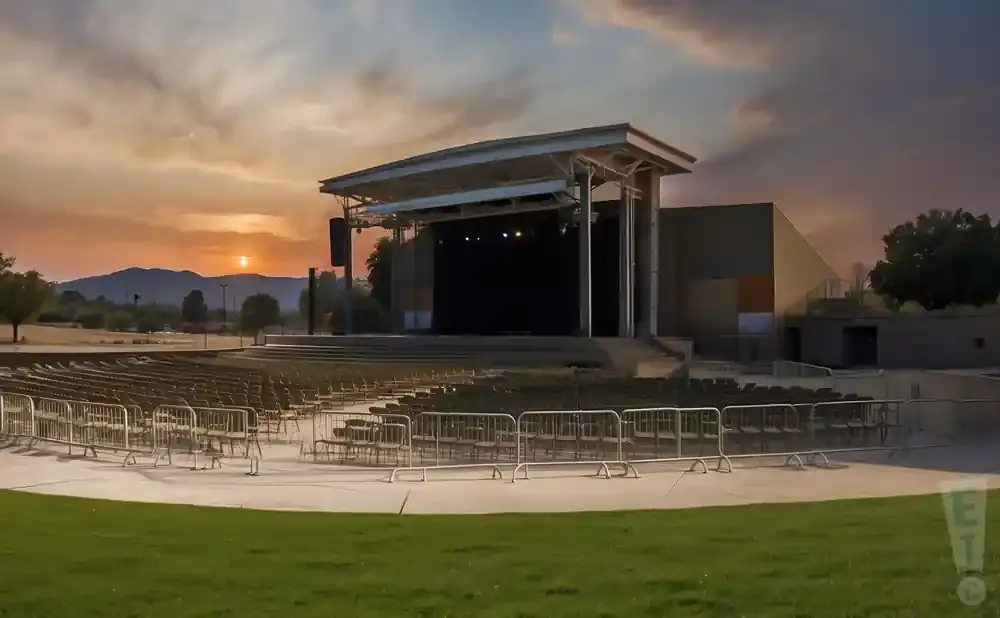An outdoor amphitheater stage at sunset, with rows of empty seats and a grassy foreground.