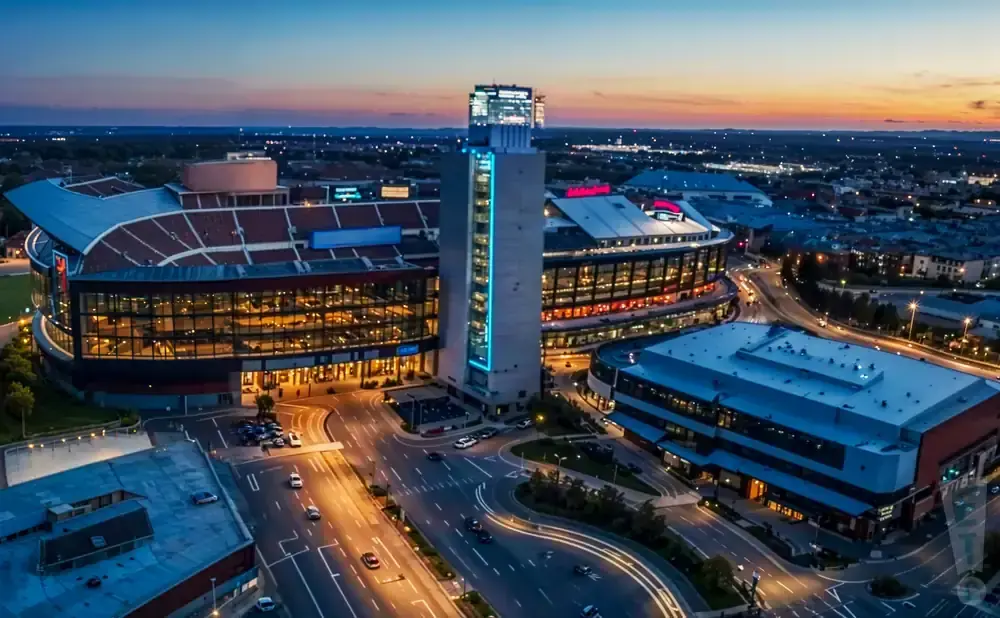Aerial view of a modern stadium complex at dusk, with illuminated buildings and roads.