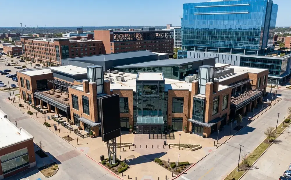 Aerial view of a modern brick building with a glass entrance and a high-rise glass building in the background.