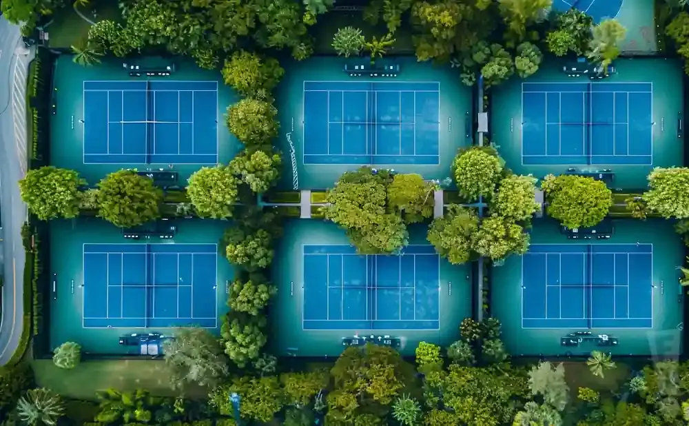 Aerial view of six blue tennis courts surrounded by lush green trees.