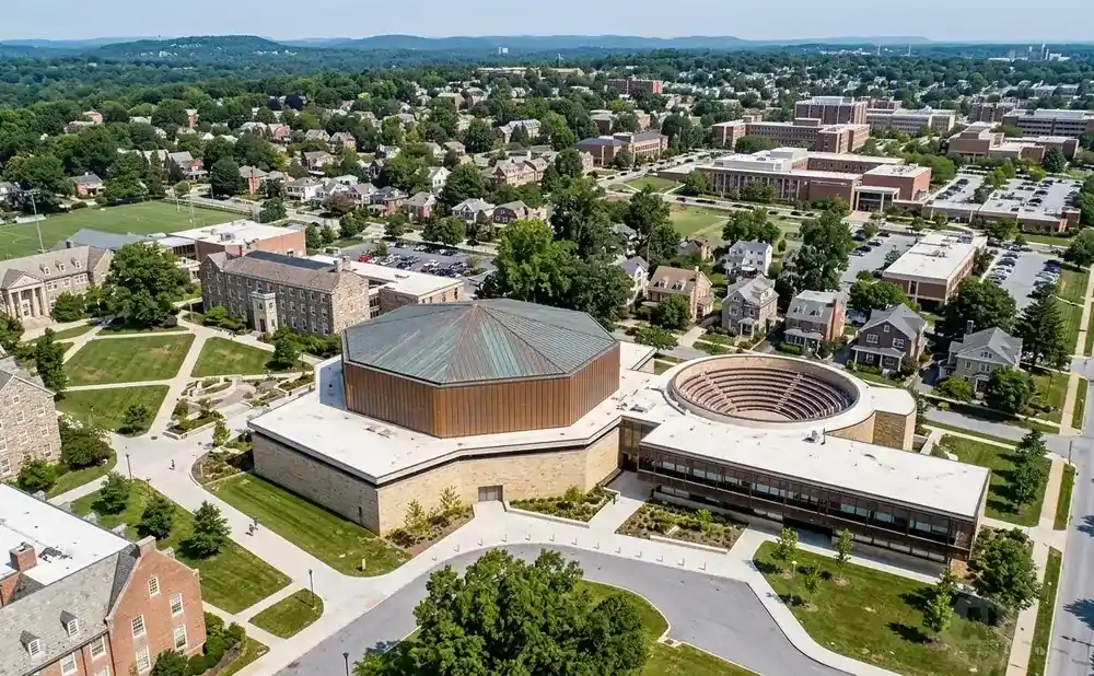 Aerial view of a university campus with various buildings, green spaces, and surrounding trees.