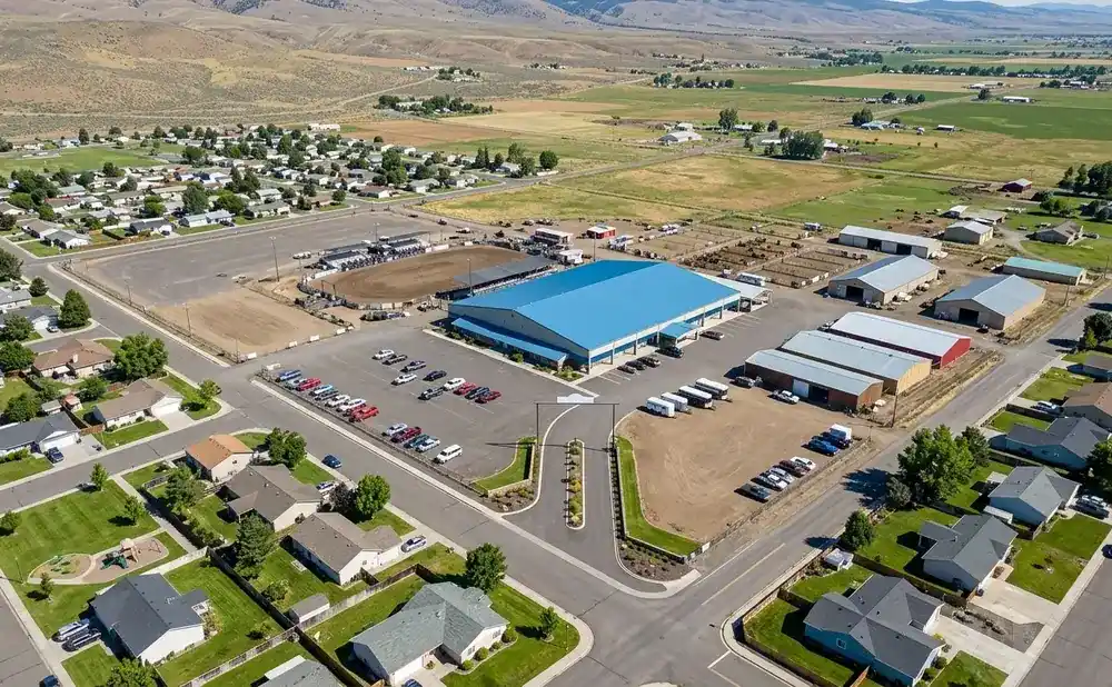 Aerial view of a community with a large blue building, rodeo arena, housing, and agricultural facilities.