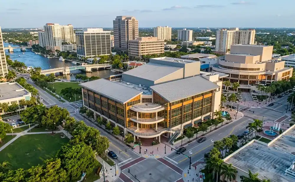 Aerial view of a modern performing arts center and surrounding buildings in a city with a river and bridges.
