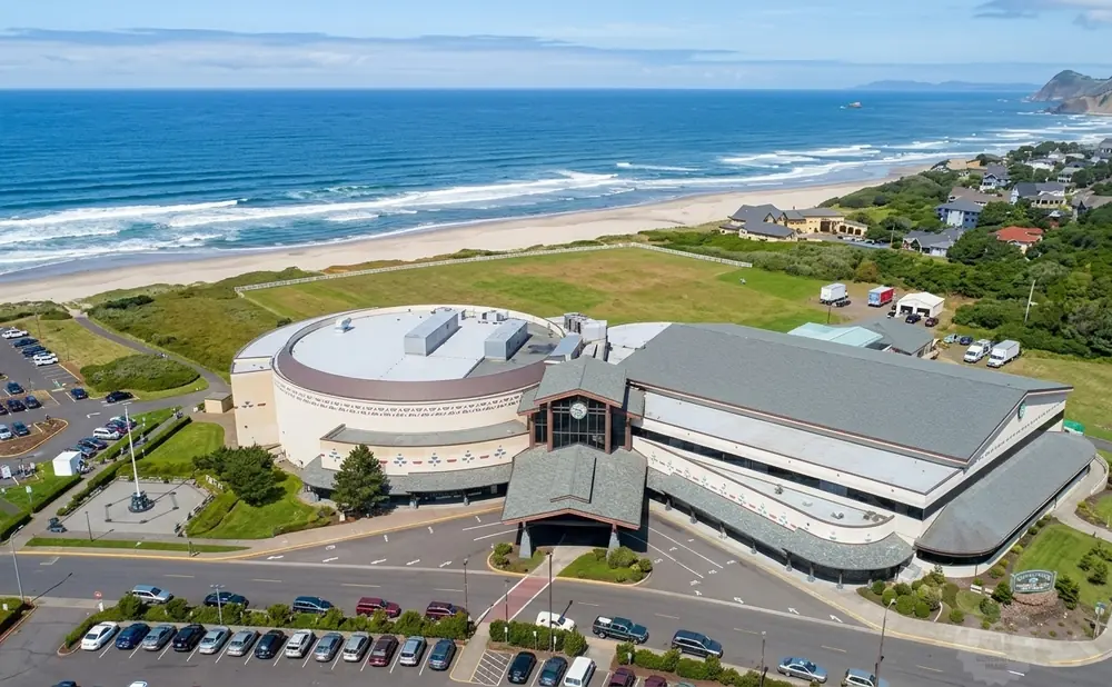 Aerial view of a large casino and hotel complex on the Oregon coast, with the Pacific Ocean and beach in the background.