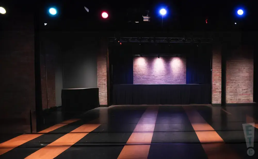 A dimly lit stage with brick backdrop and purple spotlights.