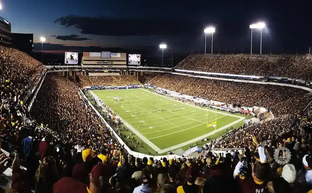A nighttime football game at a packed stadium with bright lights and a vast crowd.