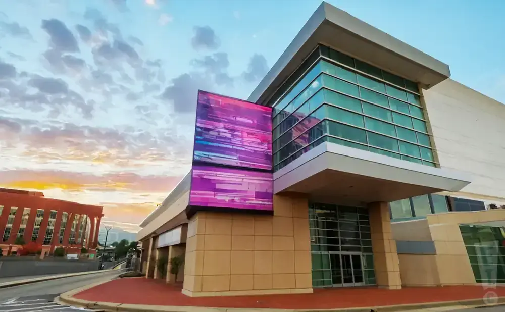 Modern building with a large glass facade and a colorful digital display at sunset.