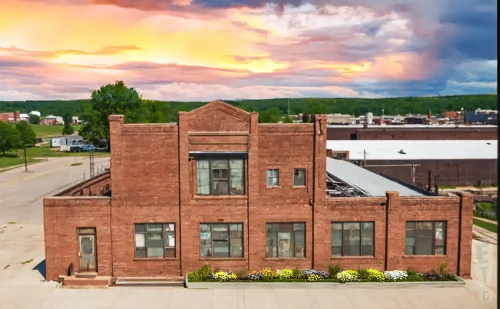 Drone view of a brick building with a broken roof under a dramatic sunset sky.