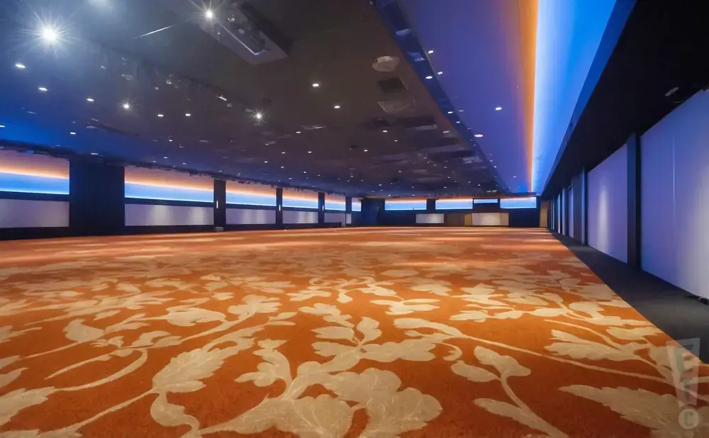 An empty convention hall with orange floral carpet, dark ceiling, and blue/orange accent lighting.