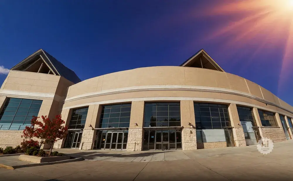 Wide shot of a tan building with large glass windows, under a bright blue sky with sun flares.