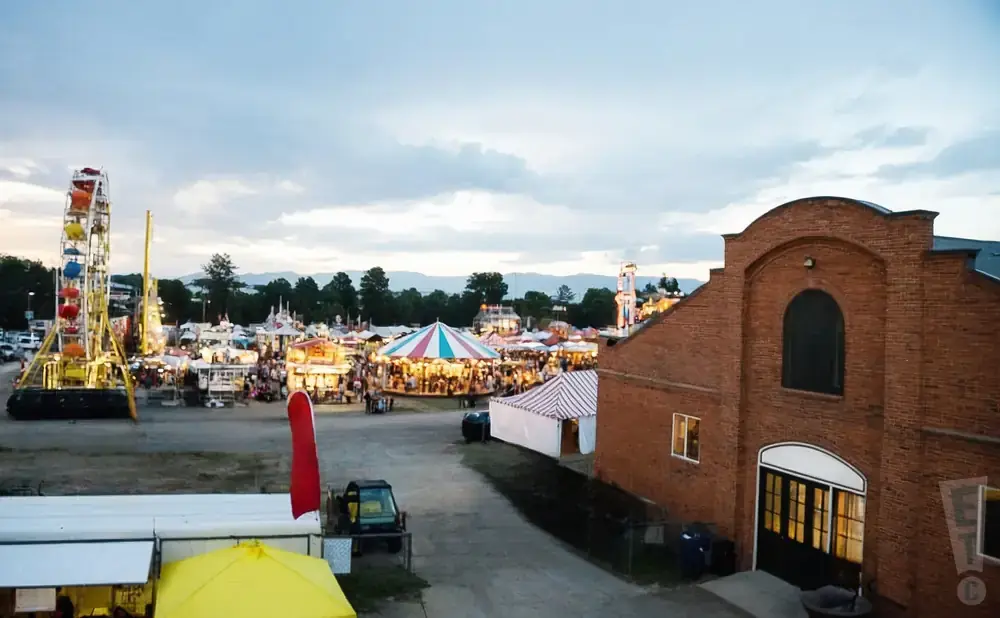 A fairground with rides, tents, and a brick building under a cloudy sky.