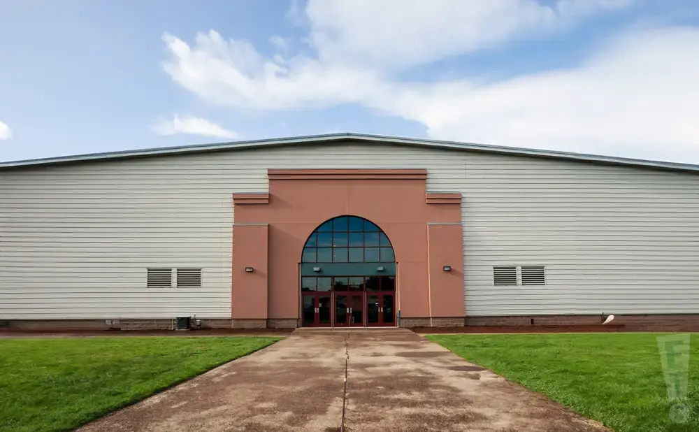 A large building with a light-colored metal exterior and a prominent arched entryway with glass doors.