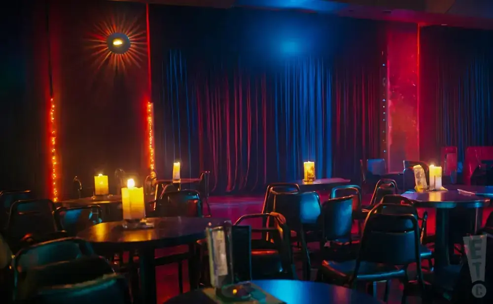 A dimly lit room with red and blue stage lights, dark curtains, and tables set with candles.