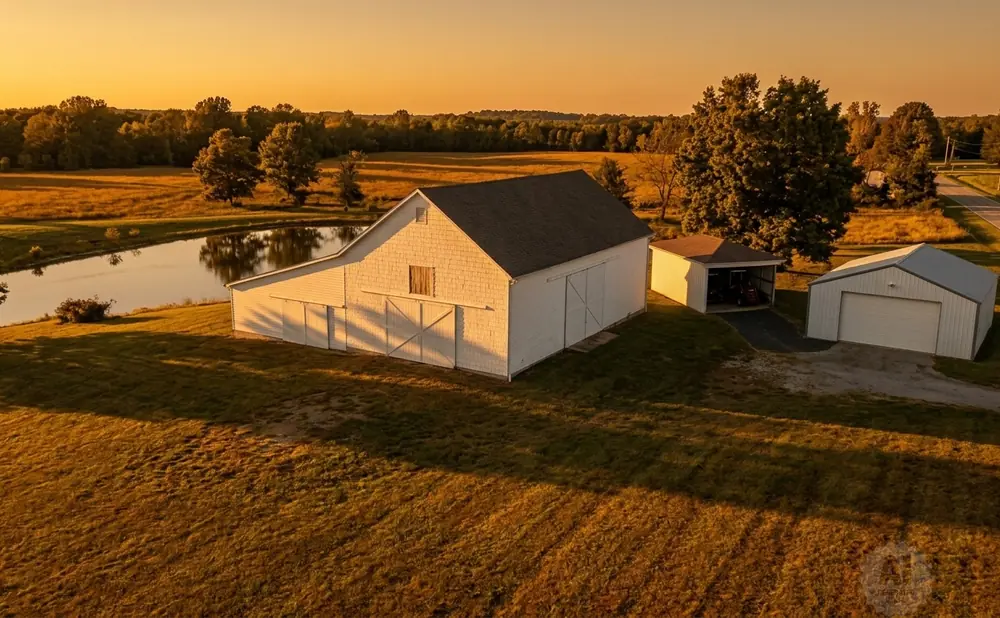 Golden hour light on a white barn, pond, and rural landscape with fields and trees.