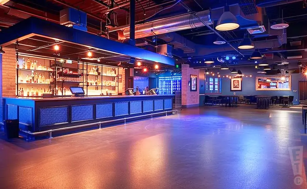Bar interior with a long bar, shelves of bottles, tables, and a dance floor.