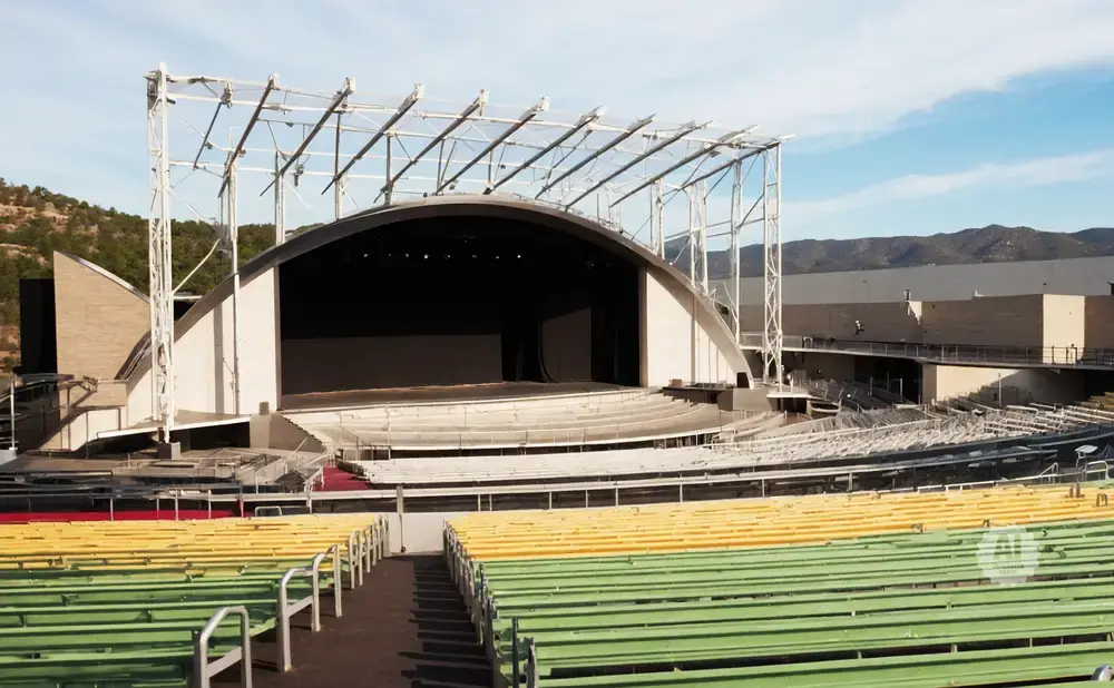 Outdoor amphitheater with a large arched stage and tiered seating, some of which is green and yellow.