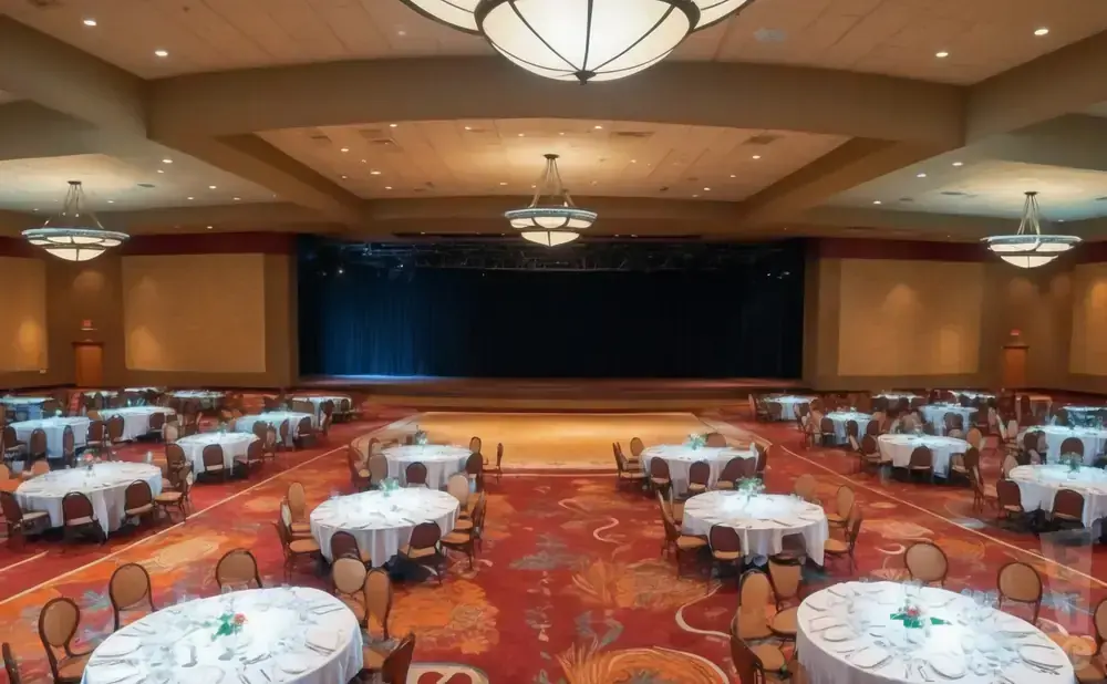 A banquet hall with round tables set for dinner and a stage at the far end.