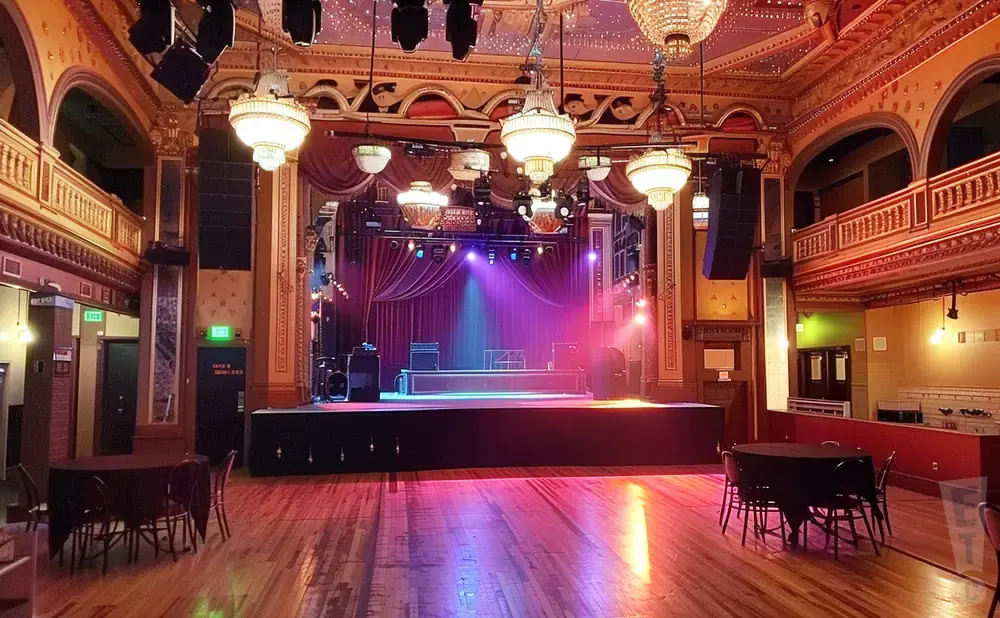 An empty concert hall with a stage, tables, and ornate decor.