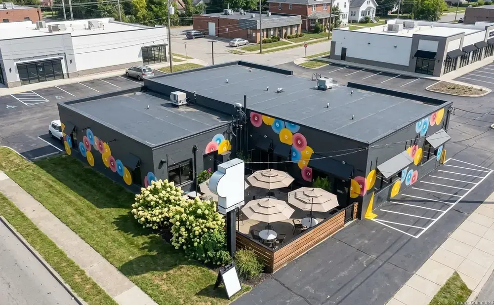 Aerial view of a dark gray building with a colorful donut mural and an outdoor patio with umbrellas.