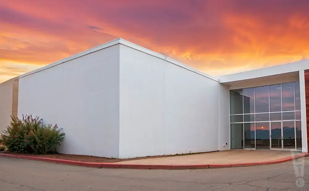 A modern building with large windows stands against a vibrant sunset sky.