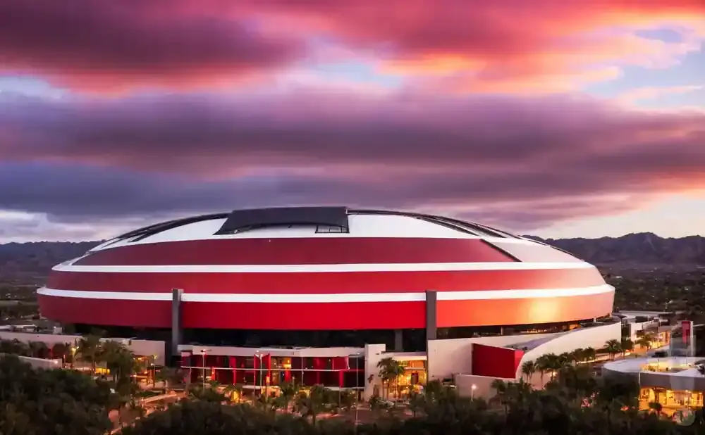A stadium with red and white bands under a dramatic purple and pink sunset sky.
