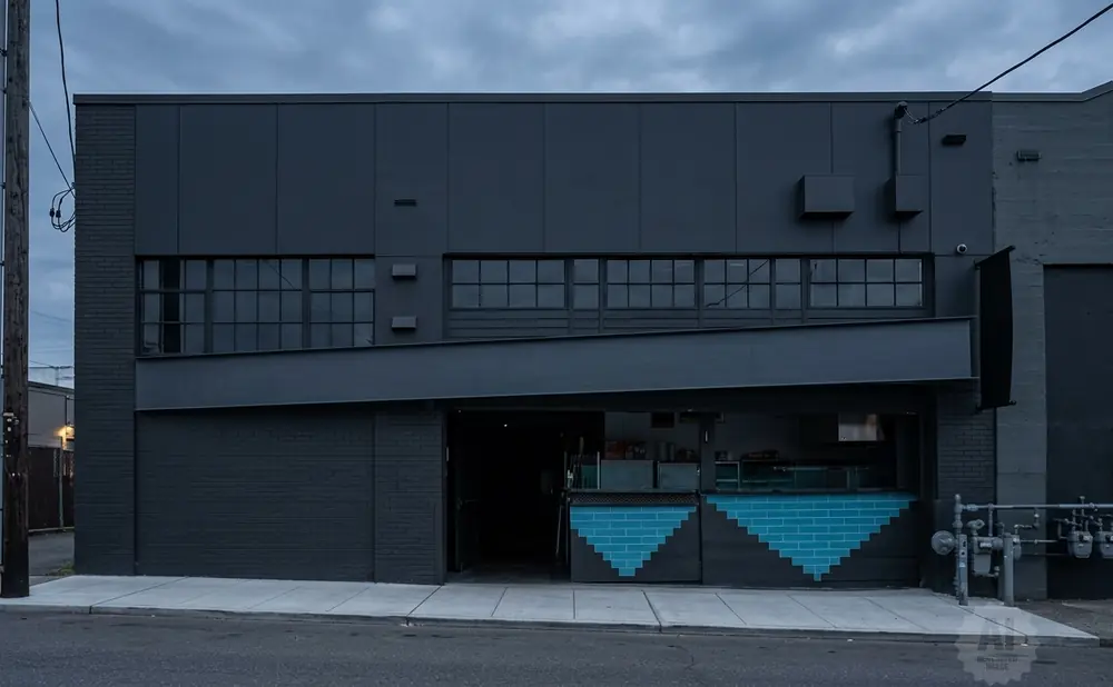 A dark, modern building with a slanted awning over an open entrance. Blue tile accents decorate the facade.