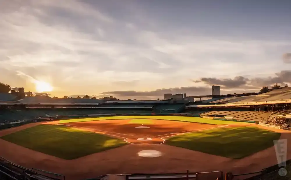 Baseball stadium at sunset with the sun setting behind the outfield bleachers.