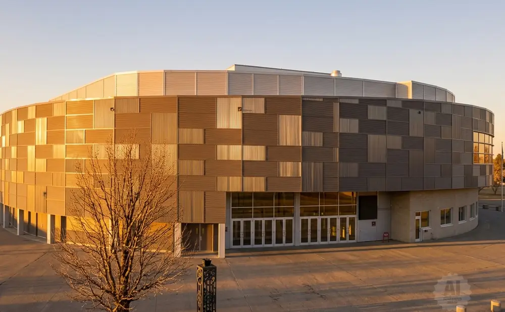 A modern, curved building with a patterned facade of metal panels in warm tones and gray, reflecting the sunset.