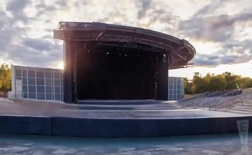 Outdoor amphitheater stage with seating and a cloudy sky.