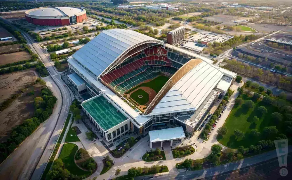 Aerial view of a baseball stadium with a retractable roof and surrounding parking lots and buildings.