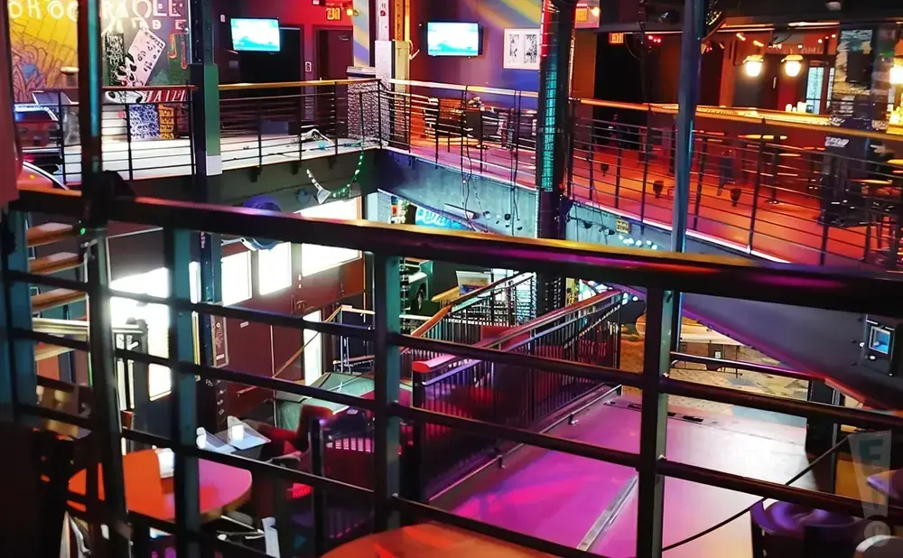 Interior view of a multi-level bar/club with railings, stairs, and neon lighting.