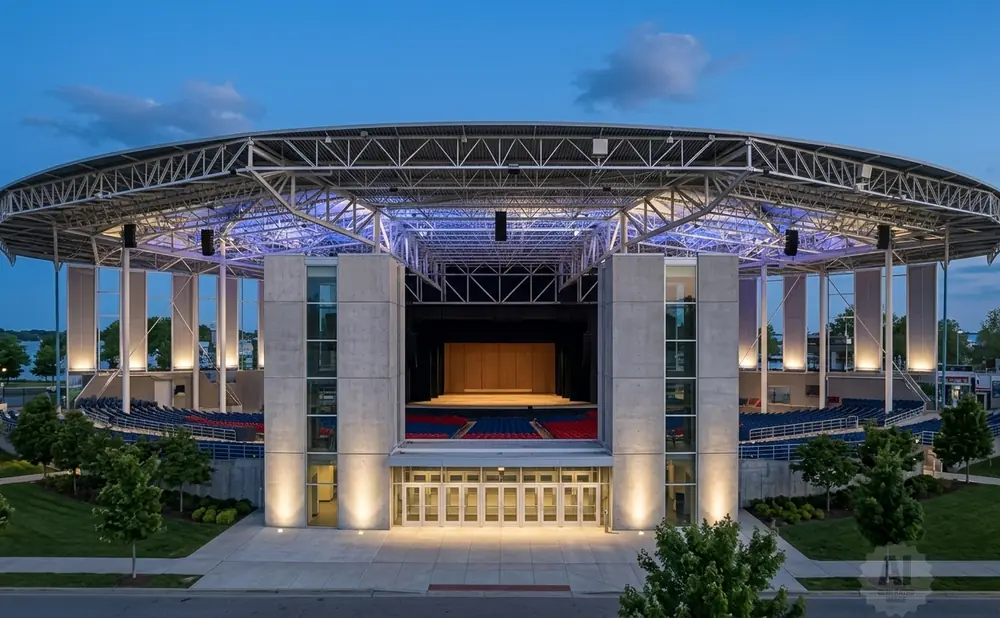 An open-air amphitheater with a curved roof, concrete pillars, and tiered seating under a twilight sky.
