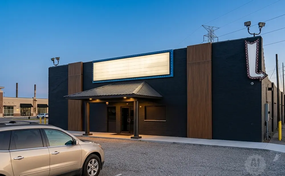 A modern building with a large illuminated sign, dark brick walls, and a covered entrance.