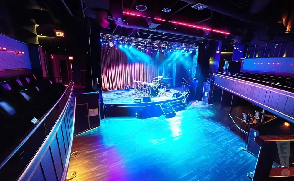 An empty concert hall stage set with drums and colorful stage lights.