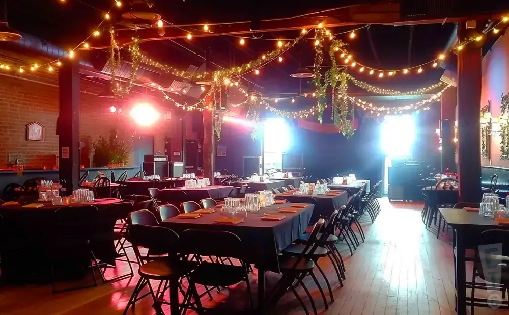 A dimly lit event space with tables set for dining, adorned with fairy lights and hanging plants.