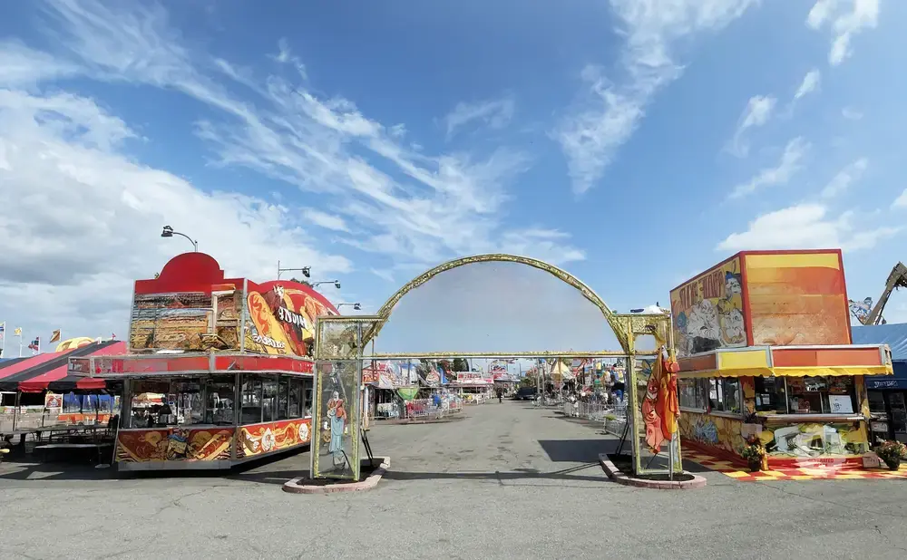 A bright, sunny day at a carnival with food stands and an arched entrance.