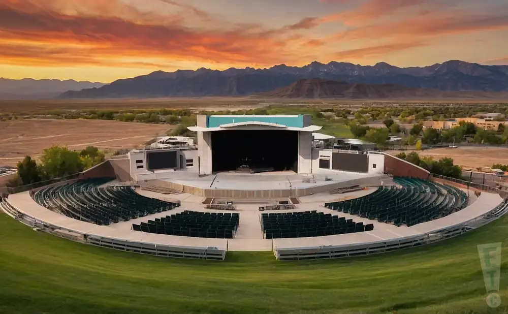Outdoor amphitheater with rows of dark green seats, a stage, and mountains under a vibrant sunset.