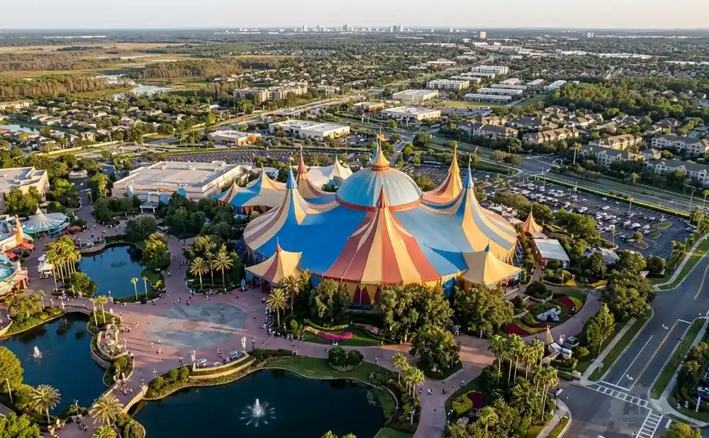 Aerial view of a colorful circus tent at a theme park with surrounding trees and buildings.