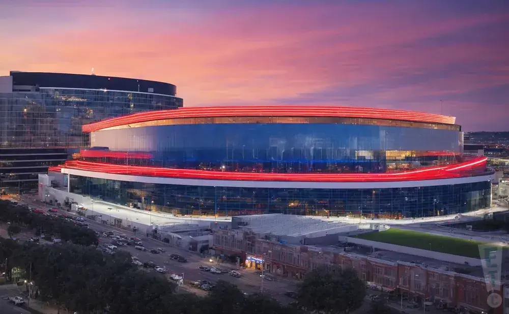 Modern stadium with glowing red accents at sunset with a sky full of pink and purple clouds.