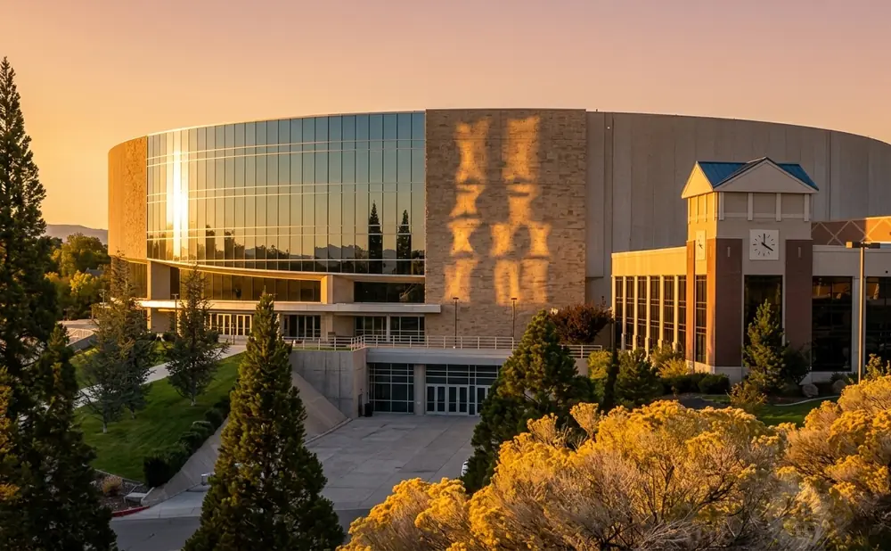 A modern, curved building with large glass windows and a stone facade, at sunset.