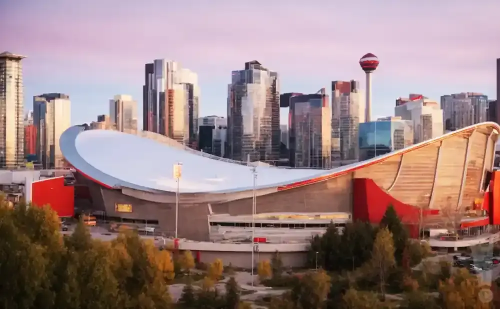 Calgary's Saddledome stadium with the downtown skyline and Calgary Tower in the background during sunset.