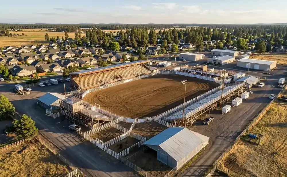 Aerial view of a rodeo arena with grandstands, surrounded by houses and trees.