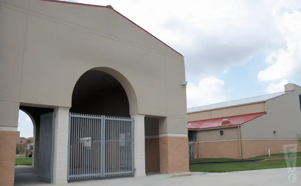 A tan building with a red roof and arched entrance with metal gates under a cloudy sky.