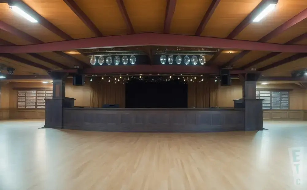 Empty ballroom with a stage, wooden floor, and ceiling beams.