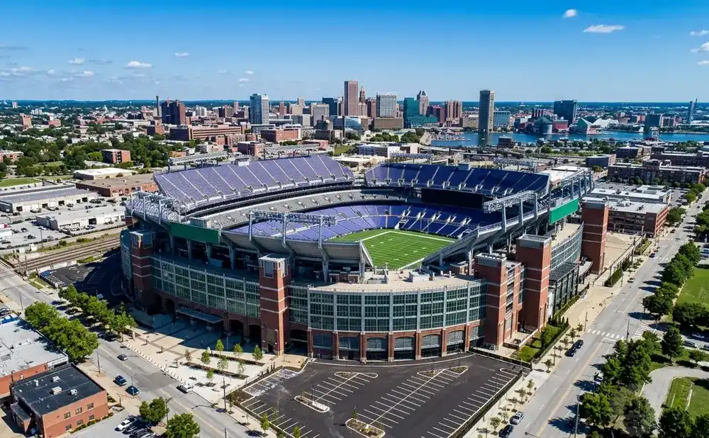Aerial view of a large, empty football stadium in a city with a skyline in the distance.