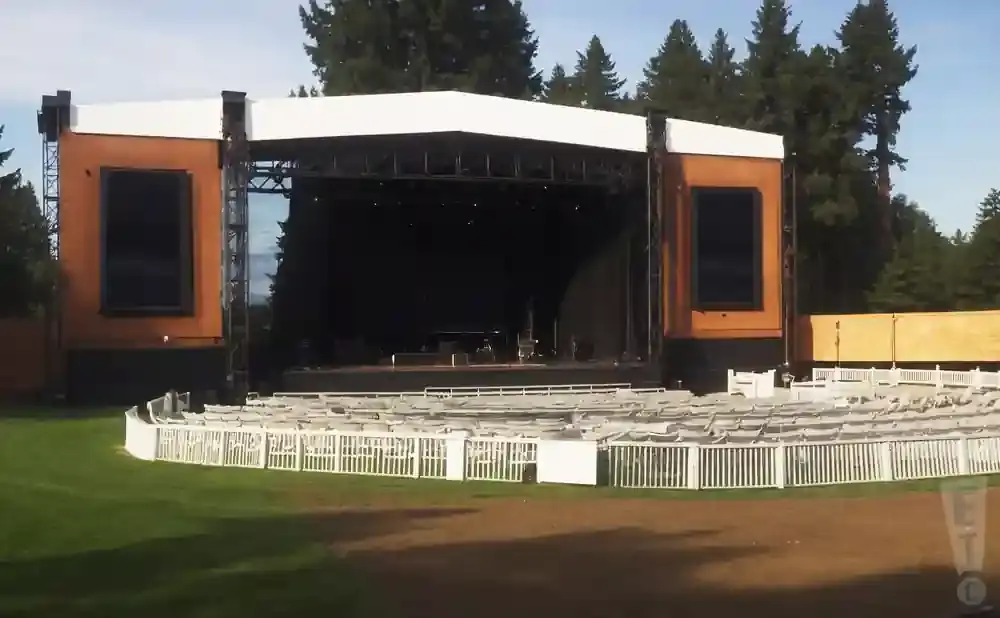 Outdoor amphitheater with a stage, seating, and trees.